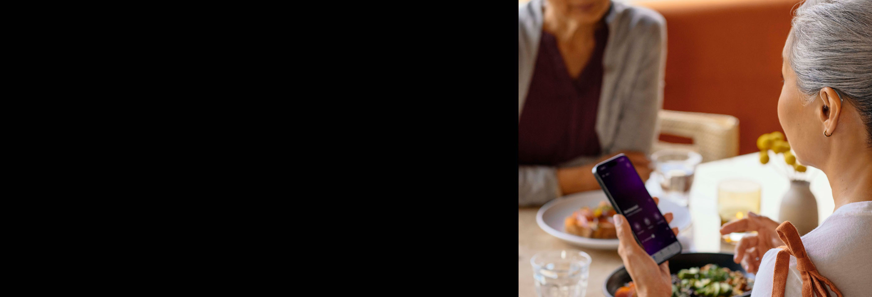 Woman sitting at a cafe controlling her hearing aids with the my starkey app.